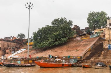 Varanasi, Uttar Pradesh, Hindistan 'daki Ganj (Ganga) nehri boyunca uzanan eski binalarla ghat' ta yaşayan Hintli insanların yüzen tekneleri ve çeşitliliği.