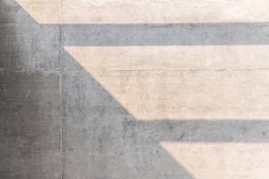 Güneş ışığı, gri beton duvar dokusuna soyut gölgeler bırakıyor..