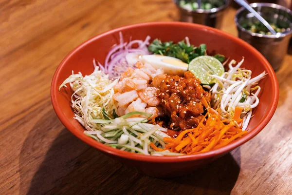 Shrimp Bibimbap Noodles, Korean noodles mixed with radish, sprout, carrot, cabbage, cucumber, boil egg and Gochujang in red bowl served with Kimchi and red chopsticks. Perfect mouth watering cuisine. — Stock Image Shrimp Bibimbap Noodles Korean Noodles Mixed Radish Sprout Carrot Cabbage Royalty Free Stock Images
