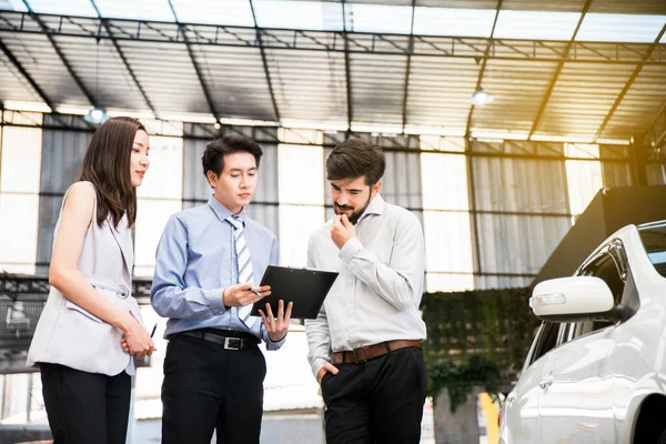 Araba galerisi. Asyalı satıcı (kadın ve erkek) teslim etmeden önce Orta Doğulu müşteri ile listeyi kontrol ediyor. Otomotiv Kiralama ve Satış Şirketi. Uluslararası İş.