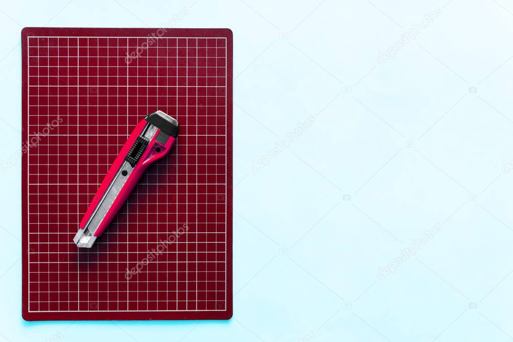Top view of red rubber cutting mat with red cutter over pale blue color paper background. Background with copy space.
