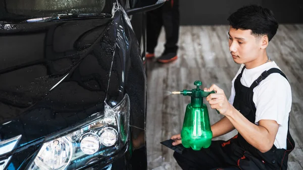 車の包装の専門家は 空気の泡を削除するには キーキーで保護するために水と手をまっすぐ包装透明フィルムを噴霧します 左フロントライトと車のフードにPpfのインストールプロセス — ストック写真