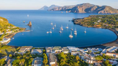 İtalya 'nın Vulcano şehrinde, Porto di Ponente' de küçük bir limanda yatları olan siyah kumlu kumsalın uçan insansız hava aracının havadan çekilmiş fotoğrafı.)