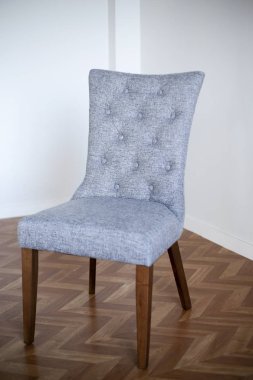 Sırtı ve kahverengi bacakları olan gri döşemeli sandalye bir ligth odasının karanlık zemininde duruyor.