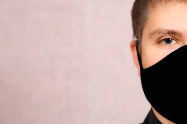 a young man in a black mask on a light background. necessary protection from covid-19. fabric reusable mask the guy does not have a part of the face in quarantine.