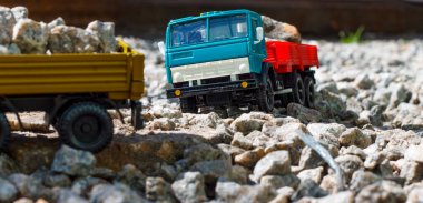 Güneşli bir günde, içi taşlarla dolu kırmızı-mavi bir Kamaz arabasının ve oyuncak römorkunun yan görüntüsü