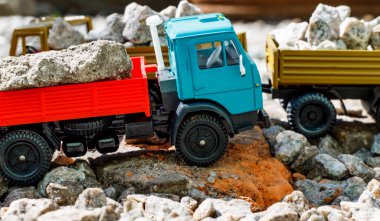 Güneşli bir günde, içi taşlarla dolu kırmızı-mavi bir Kamaz arabasının ve oyuncak römorkunun yan görüntüsü