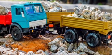 Güneşli bir günde, içi taşlarla dolu kırmızı-mavi bir Kamaz arabasının ve oyuncak römorkunun yan görüntüsü