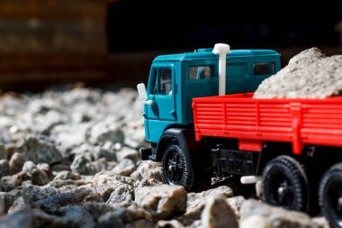 Güneşli bir günde, içi taşlarla dolu, kırmızı-mavi bir Kamaz kamyonun oyuncak modeli.