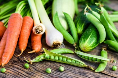 Çeşitli taze sebzeler. Bezelye, havuç, salatalık, kabak ve soğan ahşap bir masada, sağlıklı yiyecekler. Seçici odak.