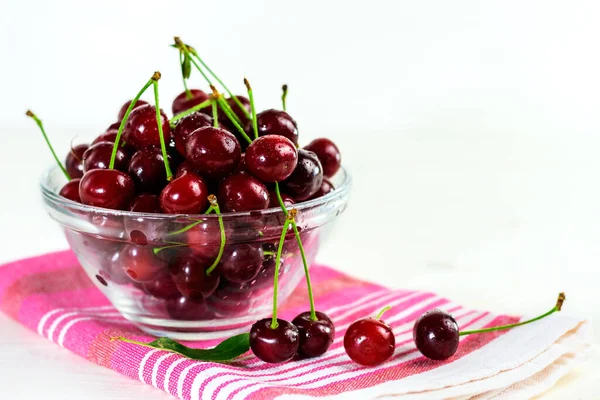 Fresh sour cherries in glass bowl, dishcloth and green leaves on wooden table. Fresh ripe sour cherries.