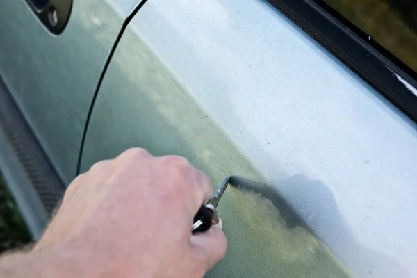 male hand scratches car wing with key