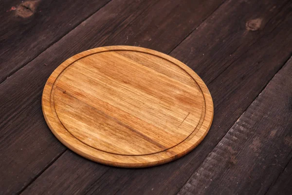Placa de corte de madeira redonda em um fundo de madeira — Fotografia de Stock