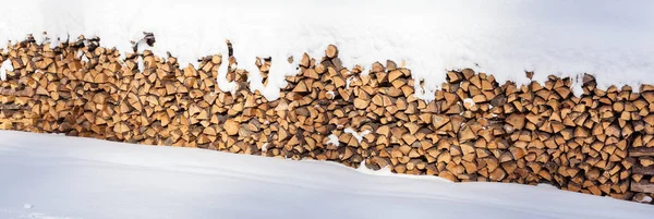 Gran pila de troncos de madera apilados en el exterior y cubiertos de nieve — Foto de Stock