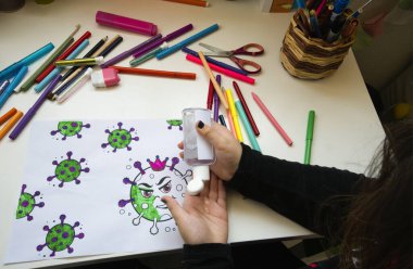 Renklerle dolu bir masaya virüsü boyayan bir çocuk ve bir şişe alkolsüz jel.