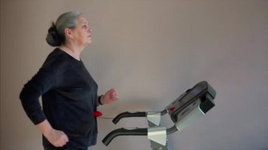Smiling senior woman walking on a treadmill. Her first training day. Safety key is used.