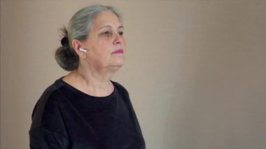 Senior woman exercising on treadmill in the home. Gray hair female use wireless headphones to listen favorite podcast.