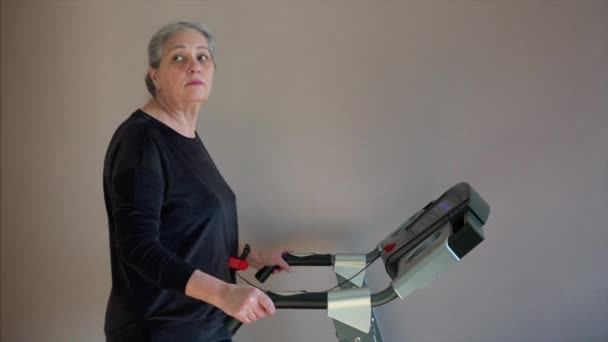 Caucasian senior woman exercising on treadmill. She is change training mode or walk speed. — Stock video