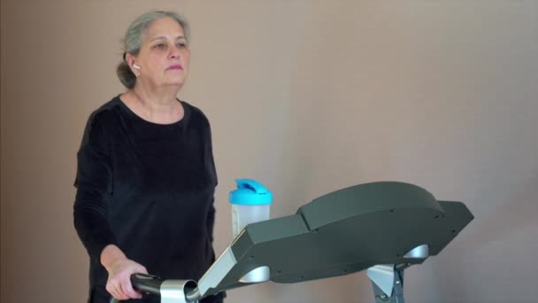 Седые волосы женщины проверить пульс использовать умные часы ходьба беговая дорожка кардио тренировки — стоковое видео