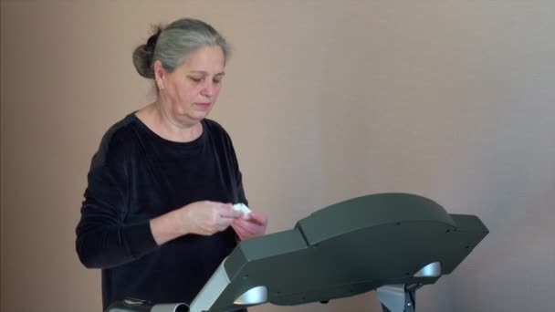 Femme cheveux gris mettre des écouteurs sans fil et marcher sur le tapis roulant — Video