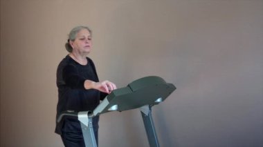 Senior Woman Exercising On Treadmill At Home Wearing Wireless Earphones