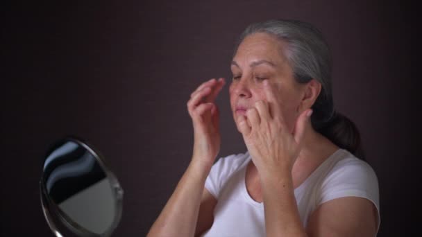 Yaşlı bir kadının portresi, berrak yüzüne yaşlanma önleyici krem sürüyor.. — Stok video