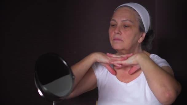 Ηλικιωμένη γυναίκα που κοιτάζει την αντανάκλαση στον καθρέφτη κάνει μασάζ προσώπου — Αρχείο Βίντεο