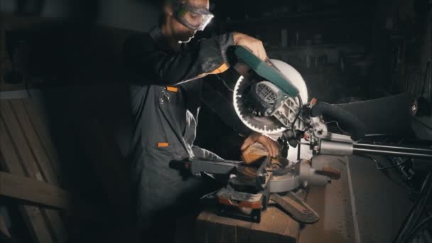 Dělník používá řezací pilu, aby zarovnal okraj prkna. Teplé světlo před námi — Stock video