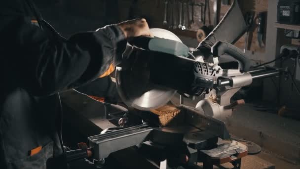 Плотник использует режущую пилу, чтобы выровнять край доски, производство мебели, низкий свет — стоковое видео