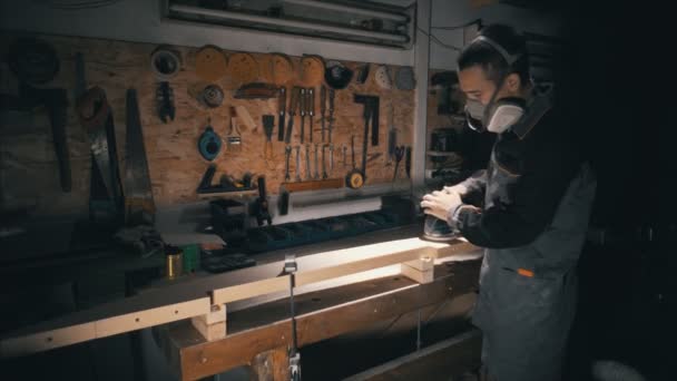 Amplia vista, carpintero puliendo una parte de madera de los muebles con una lijadora eléctrica en el taller, luz baja — Vídeos de Stock