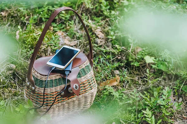 Mock up of a smartphone with charging Power Bank on a basket in the forest. Concept on the theme of outdoor recreation.