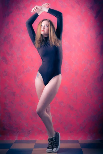 Una chica atractiva con el pelo rojo largo en un body negro y zapatillas de deporte — Foto de Stock