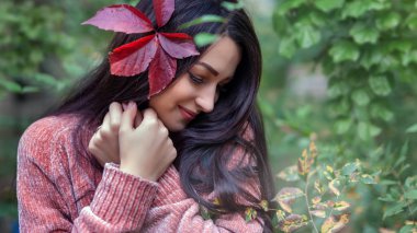 Genç esmer kız yeşilliklerin arasında yürüyor.