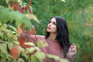 Genç esmer kız yeşilliklerin arasında yürüyor.