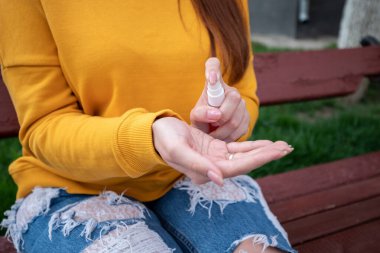 Sarı kazaklı genç bir kız ellerine sprey dezenfektan sıkar.