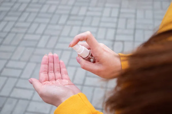 Sarı kazaklı genç bir kız ellerine sprey dezenfektan sıkar.