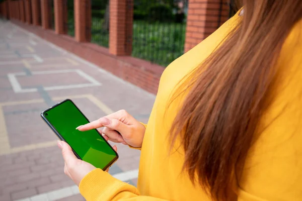 Young girl in a yellow sweater holds a phone with a green screen and scroll