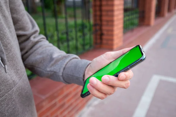 Gri kazaklı genç adam elinde yeşil ekranlı bir telefon tutuyor.