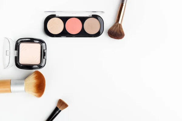 Farklı boyutlarda makyaj fırçaları ve beyaz arka planda makyaj tozu. Üst görünüm.