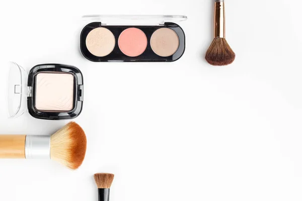 Makeup brushes of different sizes and makeup powder on a white background. Top view.
