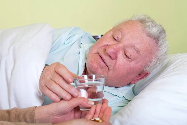Kranker alter Mann im Bett, erhält seine Tabletten — Stockfoto