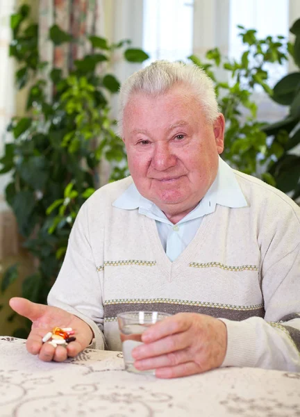 Elderly man holding pills and water — Stock Photo, Image