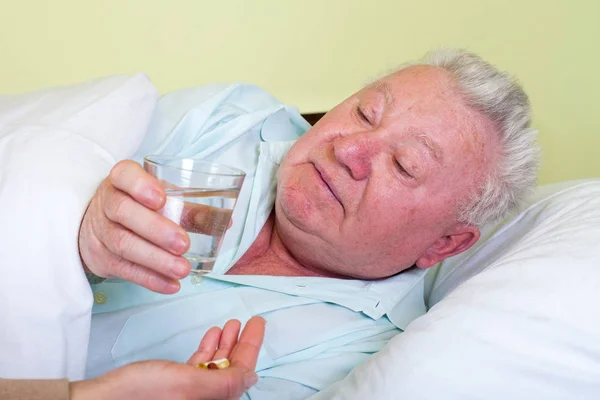 Zieke oude man in bed, het ontvangen van zijn pillen — Stockfoto