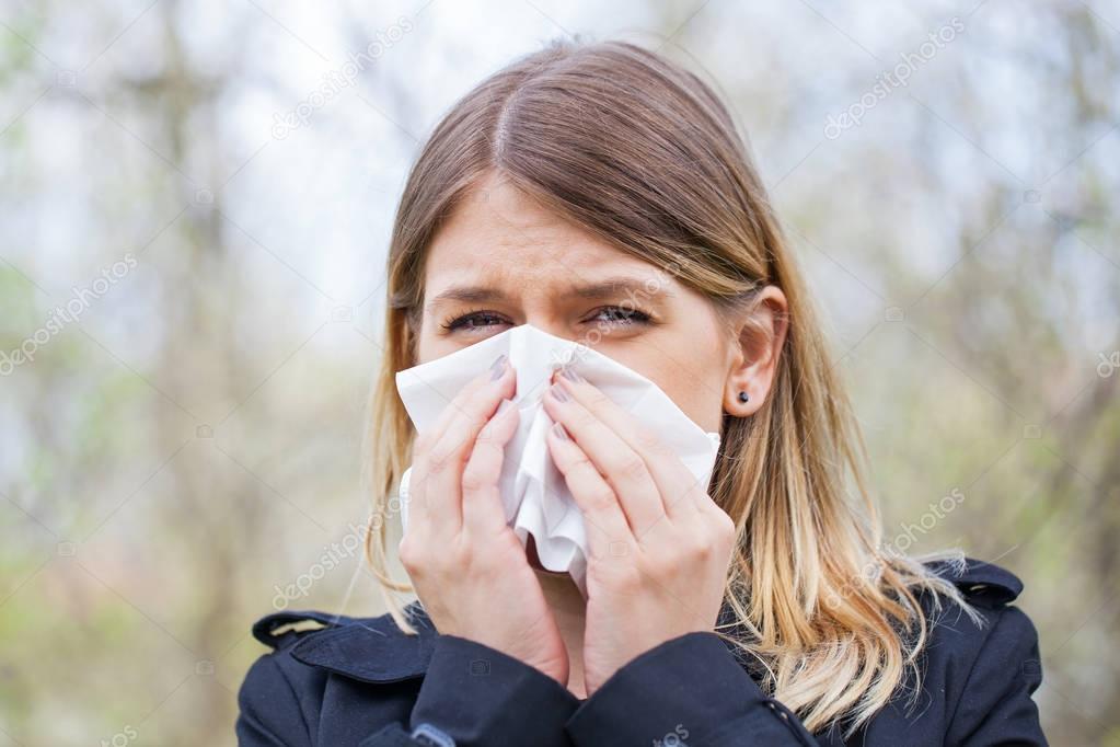 Allergic woman sneezing outdoor on springtime