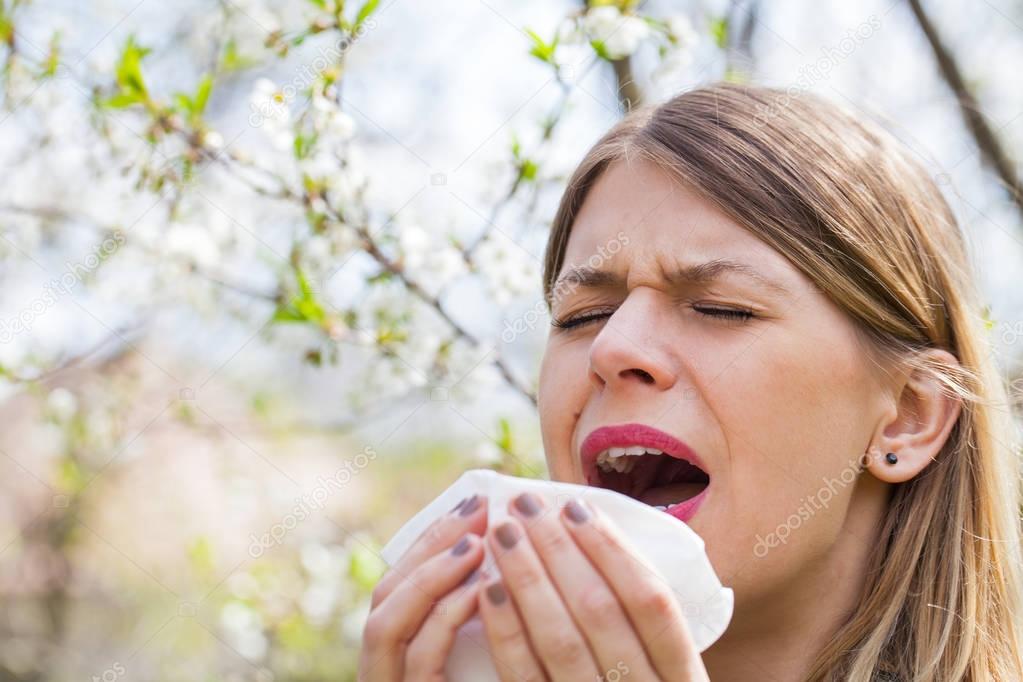 Allergic woman sneezing outdoor on springtime