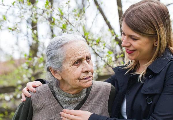 Mujer anciana con cuidador alegre al aire libre, primavera — Foto de Stock