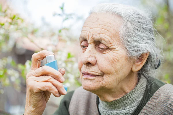 У пожилой женщины приступ астмы с бронходилататором в руках. — стоковое фото
