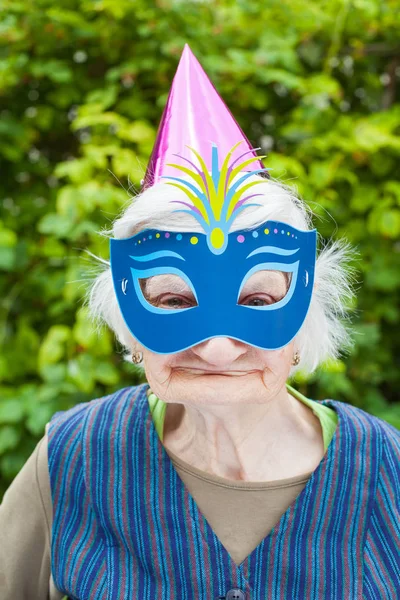 Пожилая женщина в разноцветной маске и шляпе празднует — стоковое фото