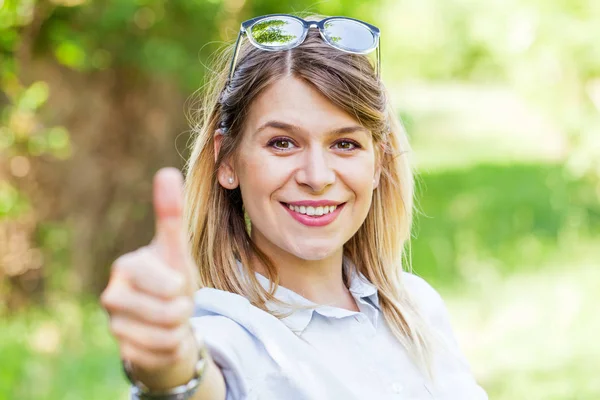Woman showing thumbs up in the park — Stock Photo, Image