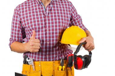 Marangoz resmi oluşturan güvenlik kask ve kulaklık, başparmak gösterilmesini tutan sarı alet kemeri ile yakın